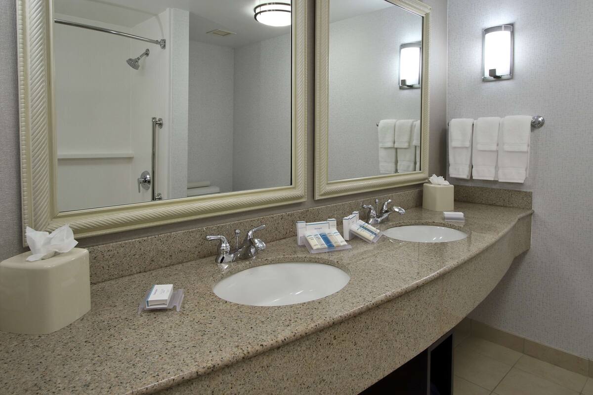 A hotel bathroom with two sinks, a large mirror, and a shower.
