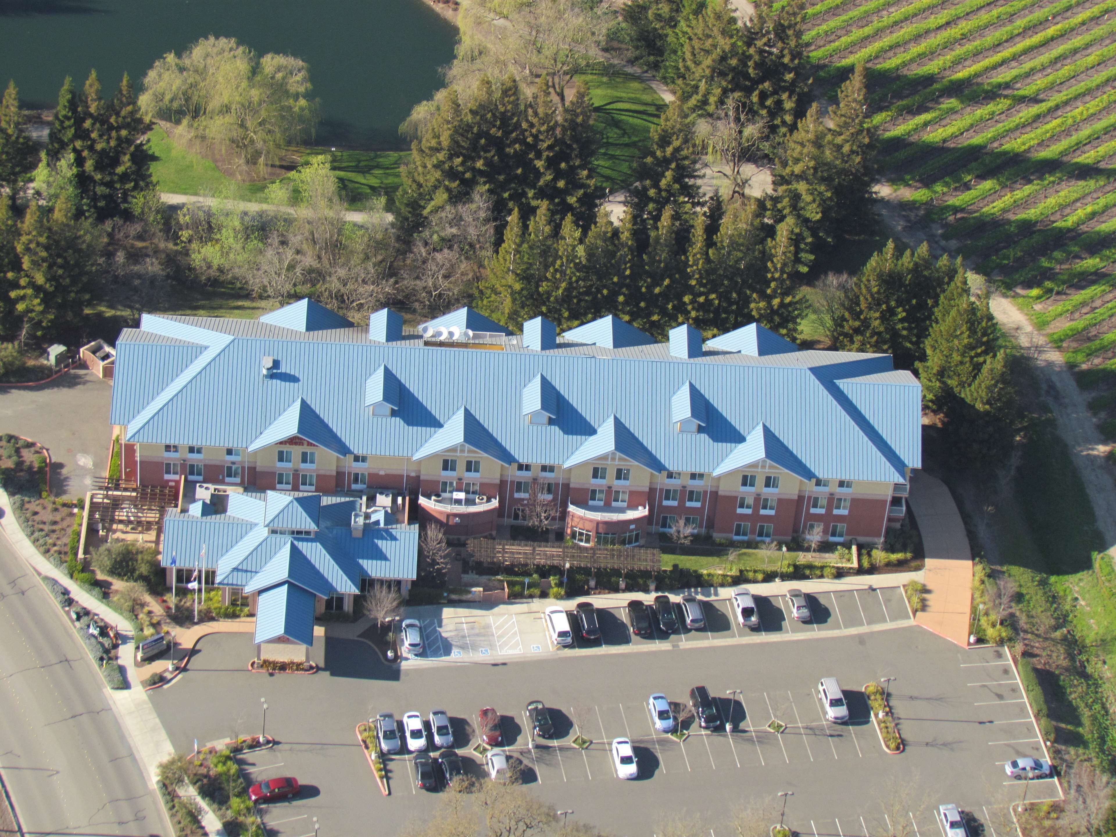 A large building with a blue roof, surrounded by a parking lot and greenery.