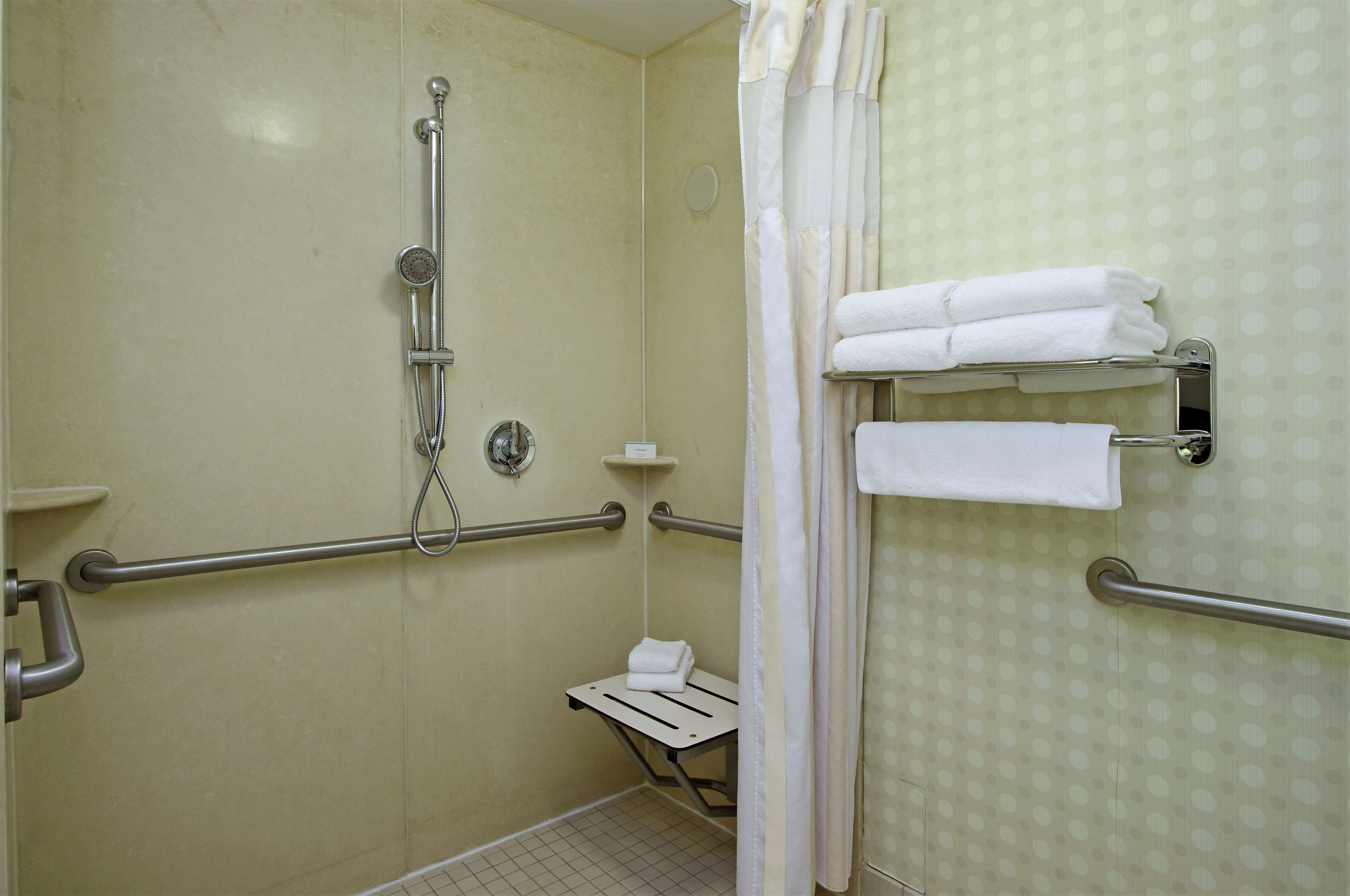 A bathroom with a shower, grab bars, a towel rack, and a toilet with a safety bar.