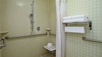A bathroom with a shower, grab bars, a towel rack, and a toilet with a safety bar.