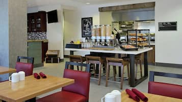 A restaurant with tables and chairs, a counter with food and drinks, and a kitchen area.