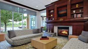 A spacious lobby with a large fireplace, a sofa, a coffee table, and a bookshelf. - Hilton Garden Inn Sonoma County Airport (Santa Rosa)