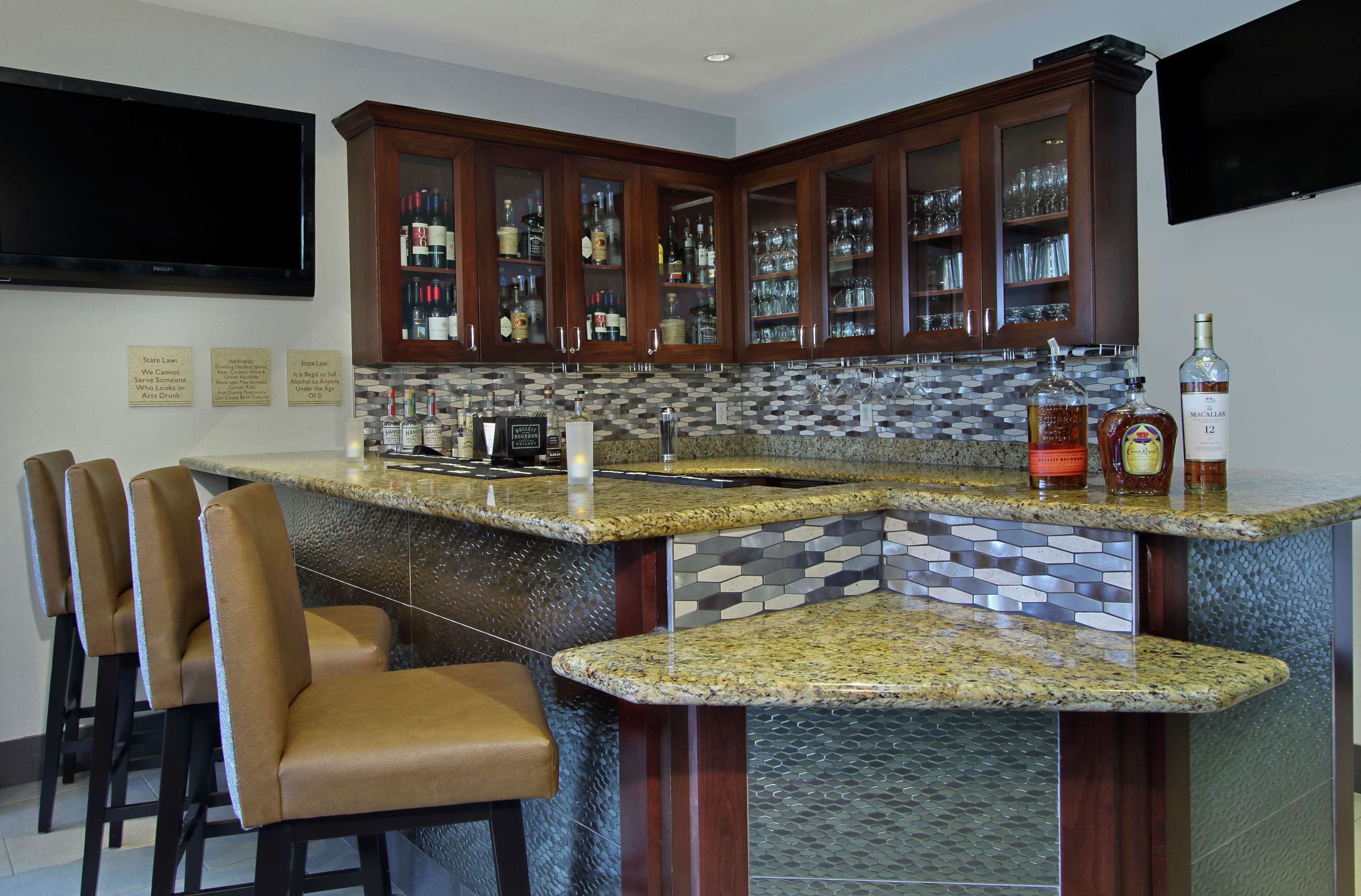 A bar area with granite countertops, bar stools, and a variety of liquor bottles.
