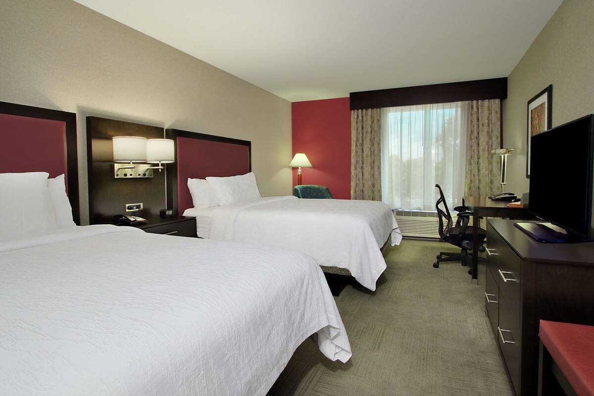 A hotel room with two beds, a desk with a computer, a chair, and a television.
