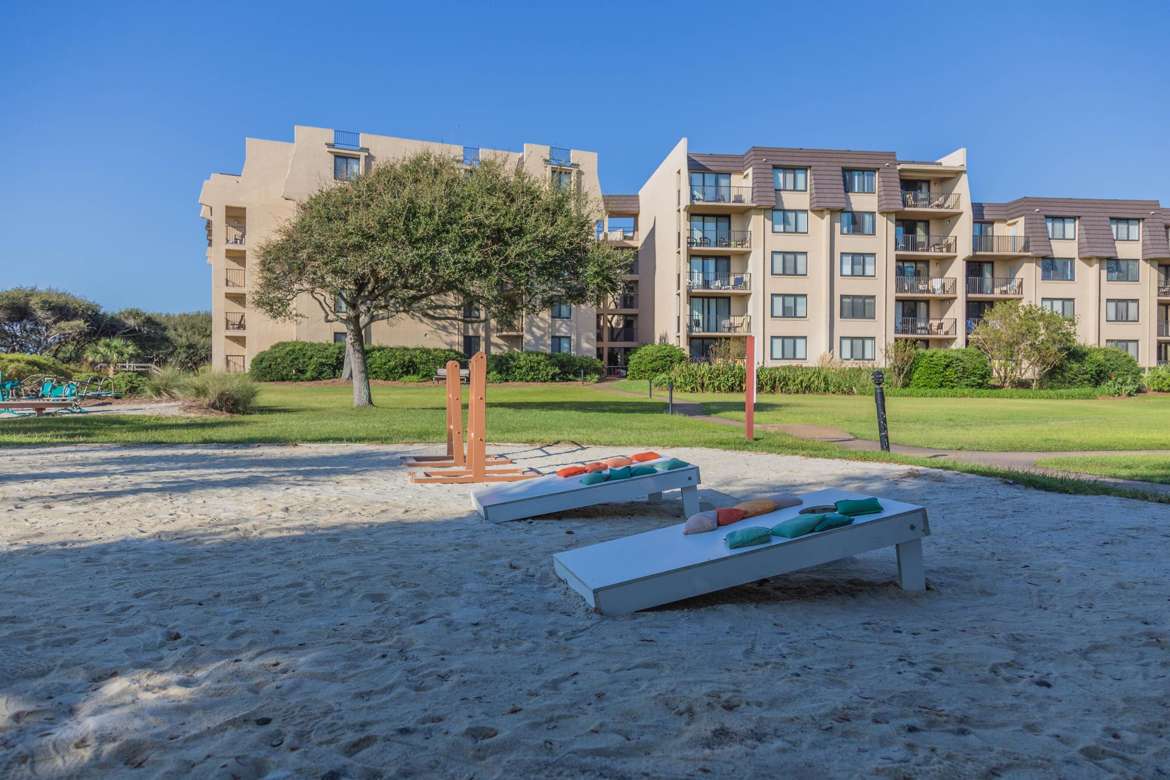 Un complexe hôtelier doté d’une plage de sable, de chaises longues et d’un grand bâtiment comportant de nombreux balcons.