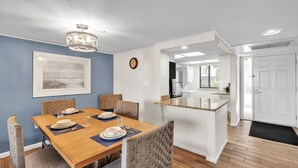 A dining area with a wooden table, wicker chairs, and a chandelier. There is a kitchen visible in the background. - Seawatch at Island Club (Hilton Head Island)