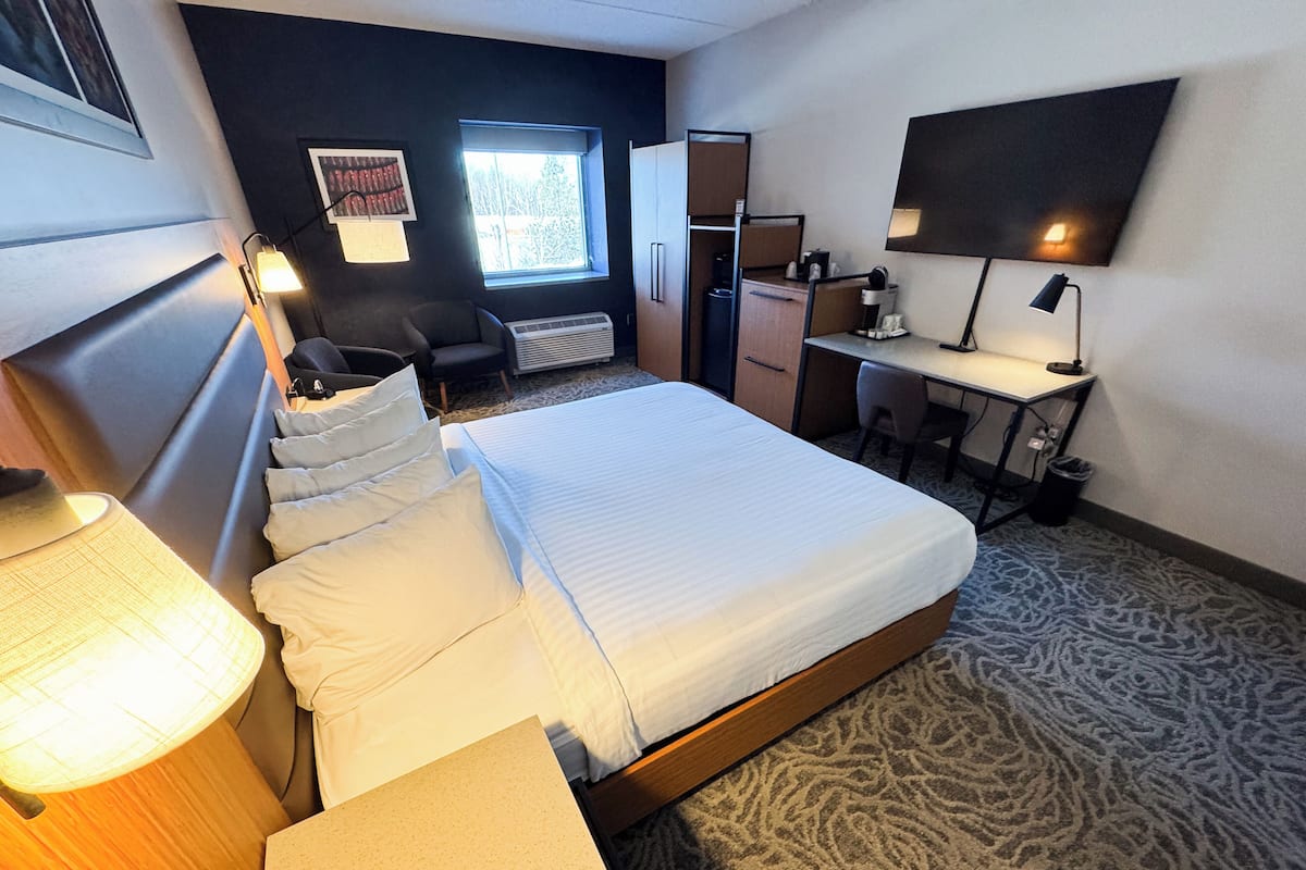 A hotel room with a bed, desk, chair, and a TV on the wall.