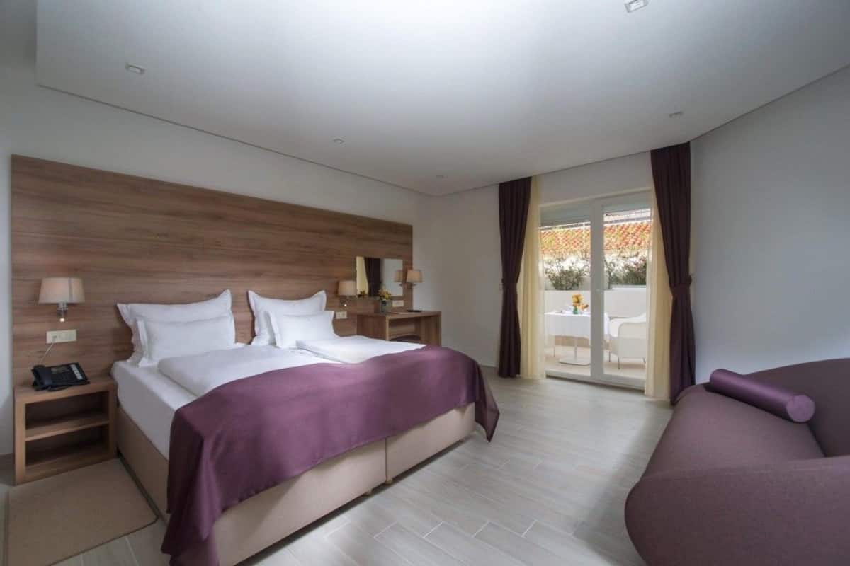 Moderni hotellihuone, jossa on suuri sänky, puinen pääty, työpöytä lampun kanssa ja näkymä ulos.