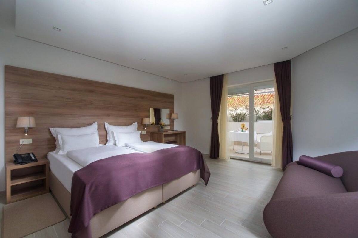 Moderni hotellihuone, jossa on suuri sänky, yöpöydät, sohva ja lasiovesta avautuva näkymä.