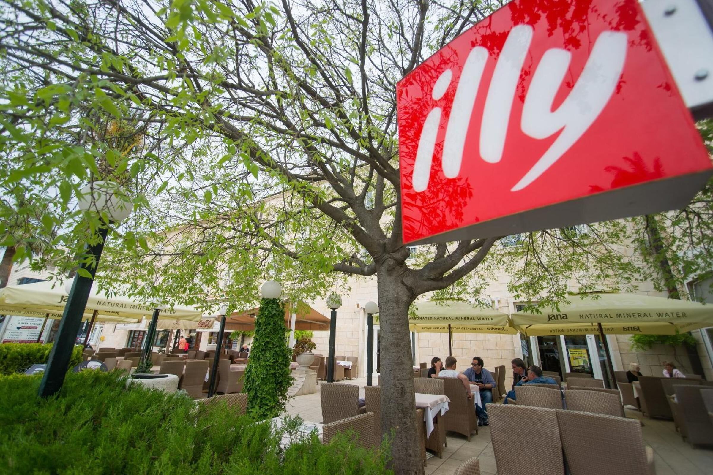 An outdoor seating area with wicker furniture and umbrellas, a tree, and a Coca-Cola sign.