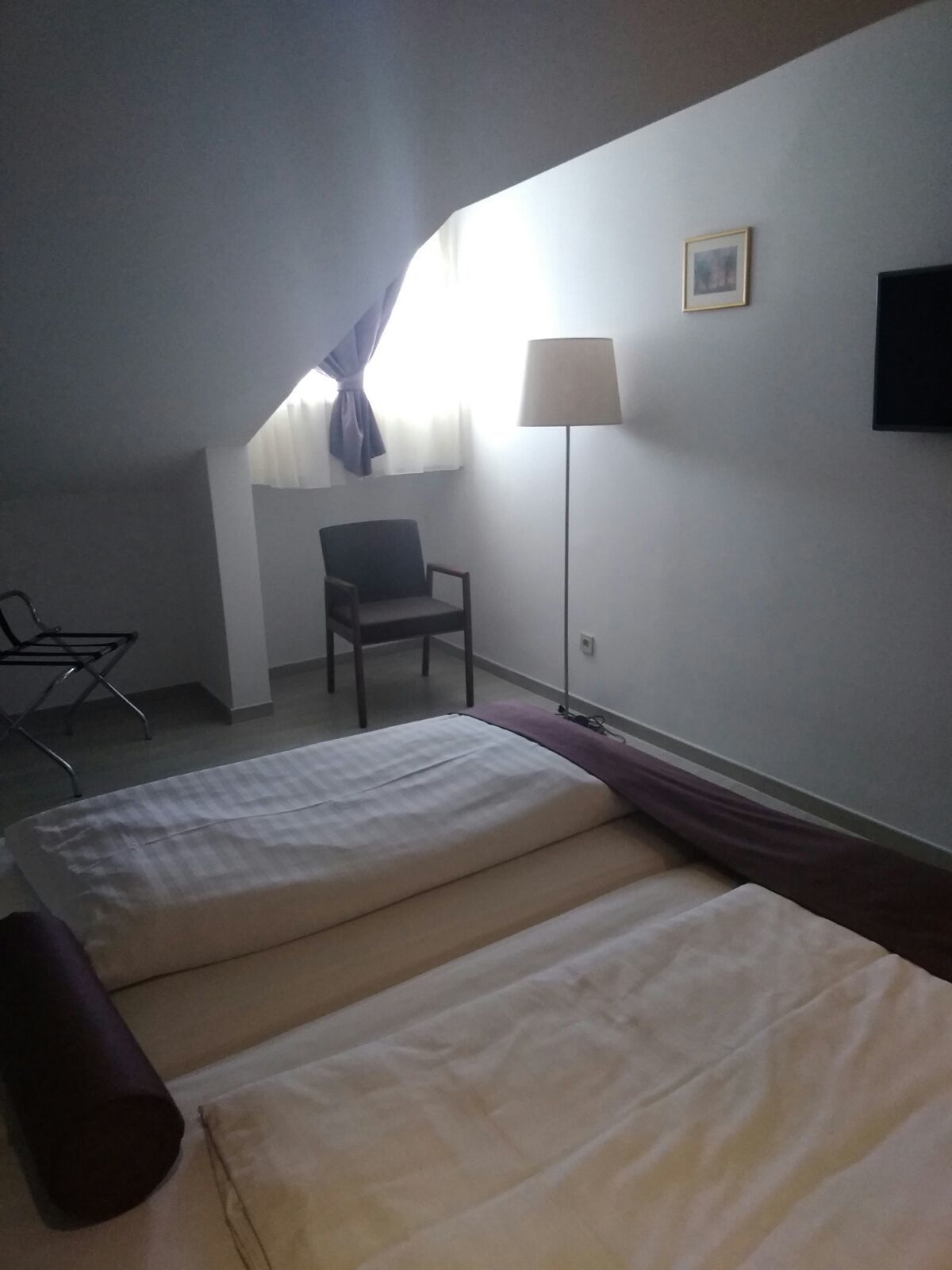 Une chambre d’hôtel avec deux lits, une chaise, un bureau, une lampe et un tableau au mur.