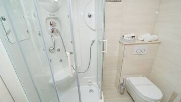 Un baño moderno con cabina de ducha de vidrio, inodoro y repisa con artículos de aseo.
