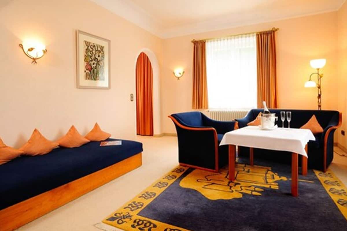 A hotel room with a sofa, two armchairs, a small table, and a decorative rug.