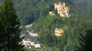 Un bâtiment qui ressemble à un château, entouré d’une forêt dense, avec un autre bâtiment plus petit à proximité.