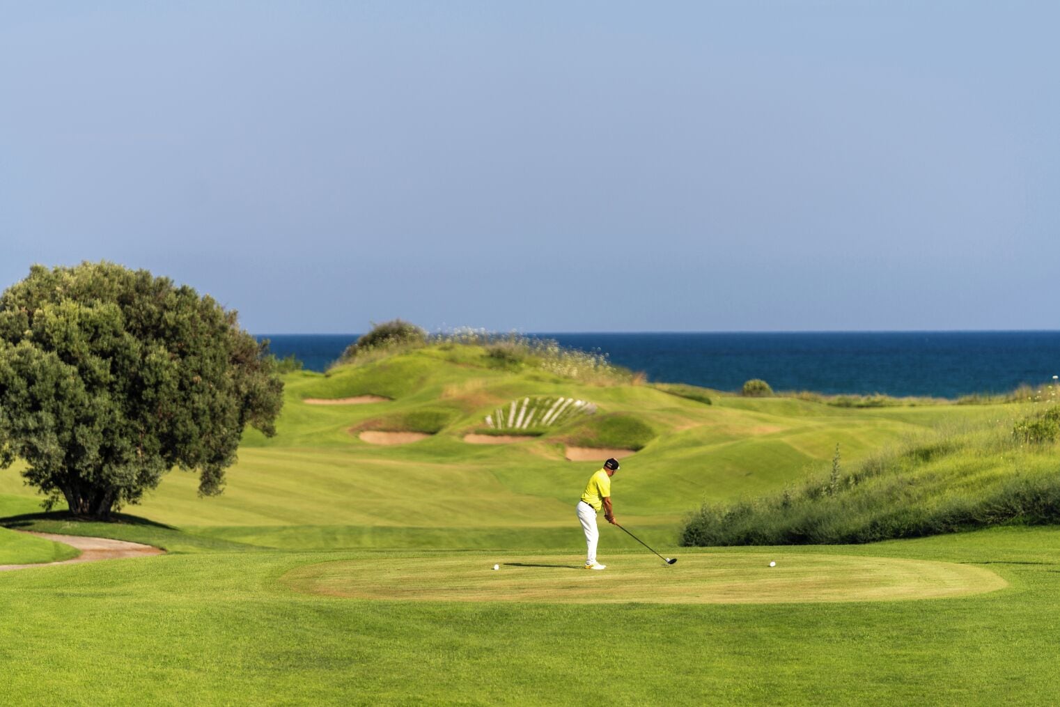 Um campo de golfe com vista clara para o oceano ao fundo.