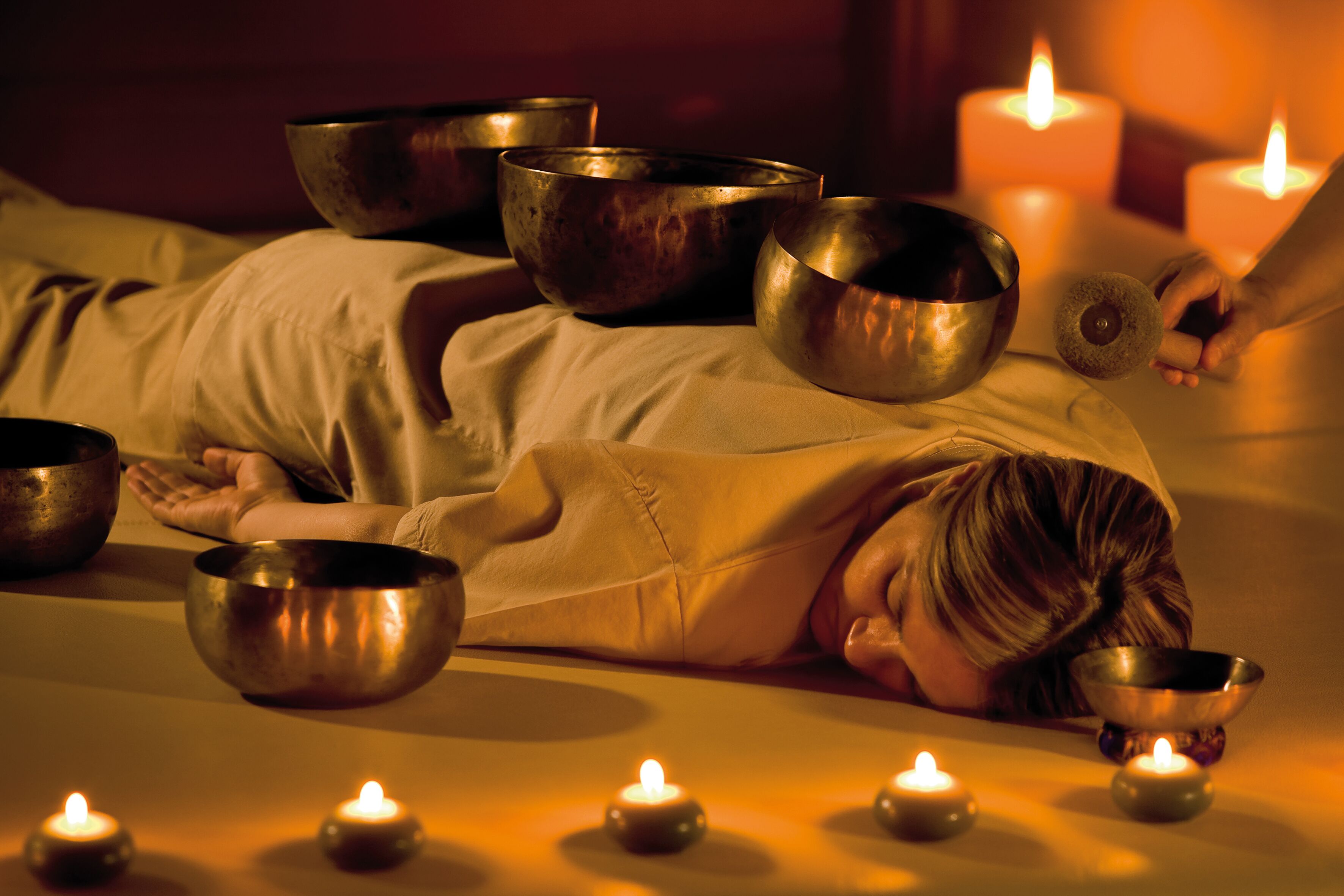 Una persona acostada en una cama con varios cuencos y velas alrededor.
