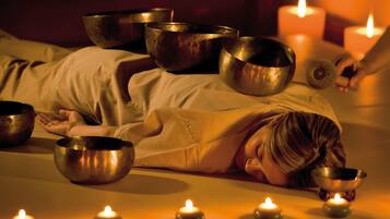 Una persona acostada en una cama con varios cuencos y velas alrededor.