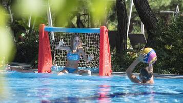 A pool area with a goal net, trees, and a person playing with a ball.