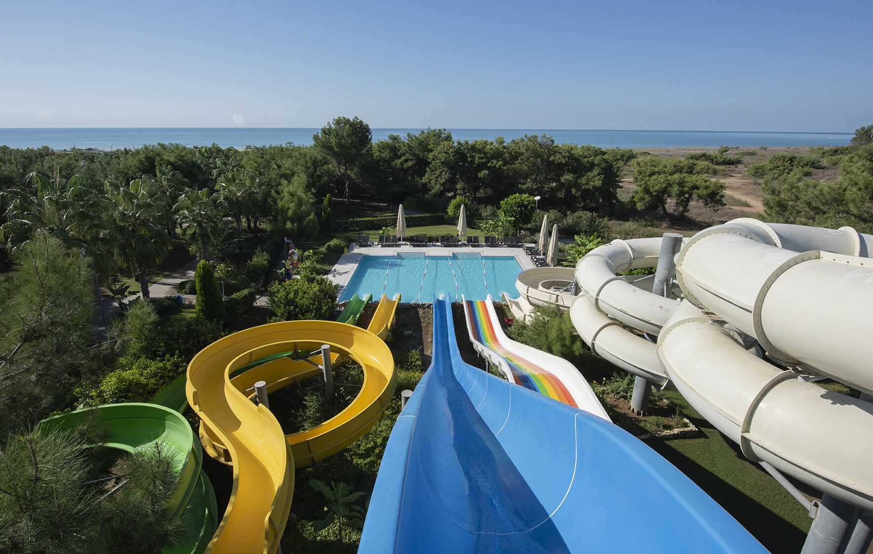 Een waterpark met glijbanen en een zwembad, omringd door bomen en een helder uitzicht op de oceaan.