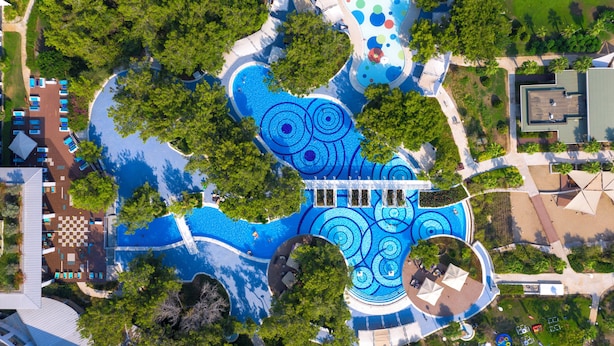 Vue aérienne d’un complexe hôtelier doté de plusieurs piscines, d’espaces ombragés et d’une végétation luxuriante.