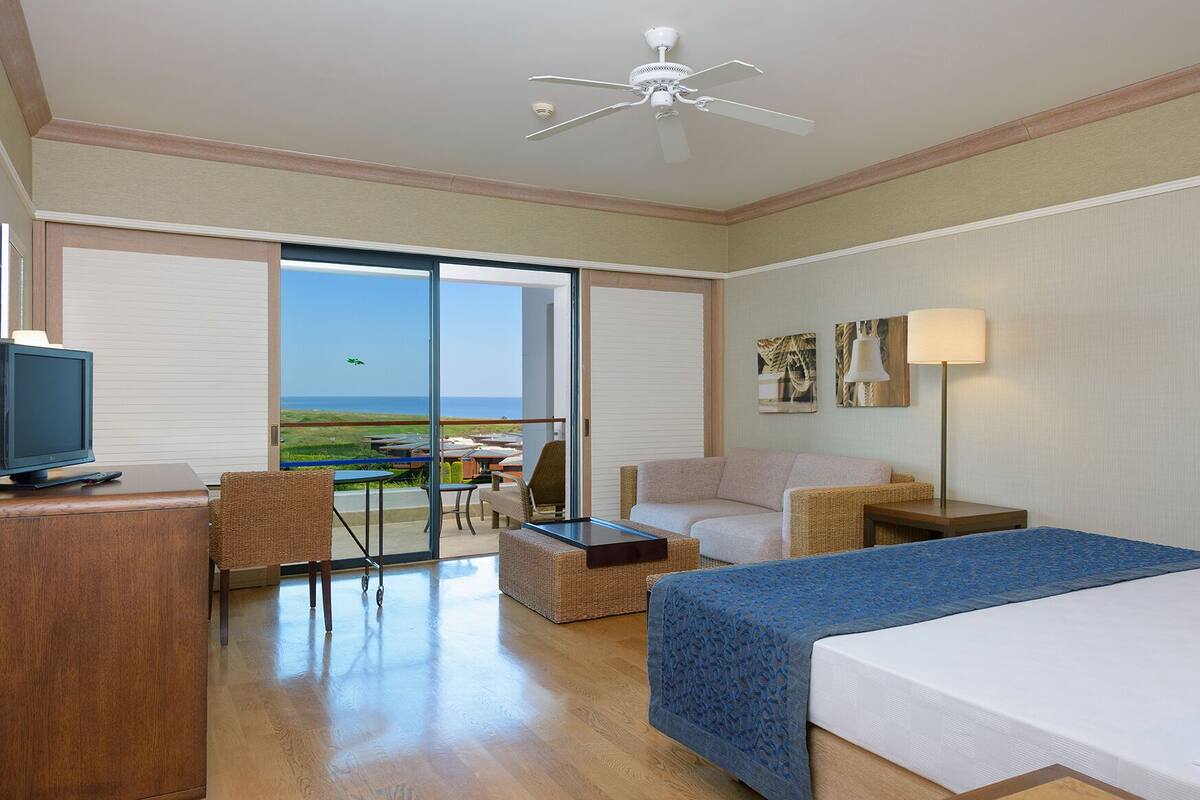 Habitación de hotel con cama, escritorio con televisor, una silla, una mesa y vista al océano.