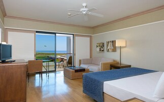Habitación de hotel con cama, escritorio con televisor, una silla, una mesa y vista al océano.