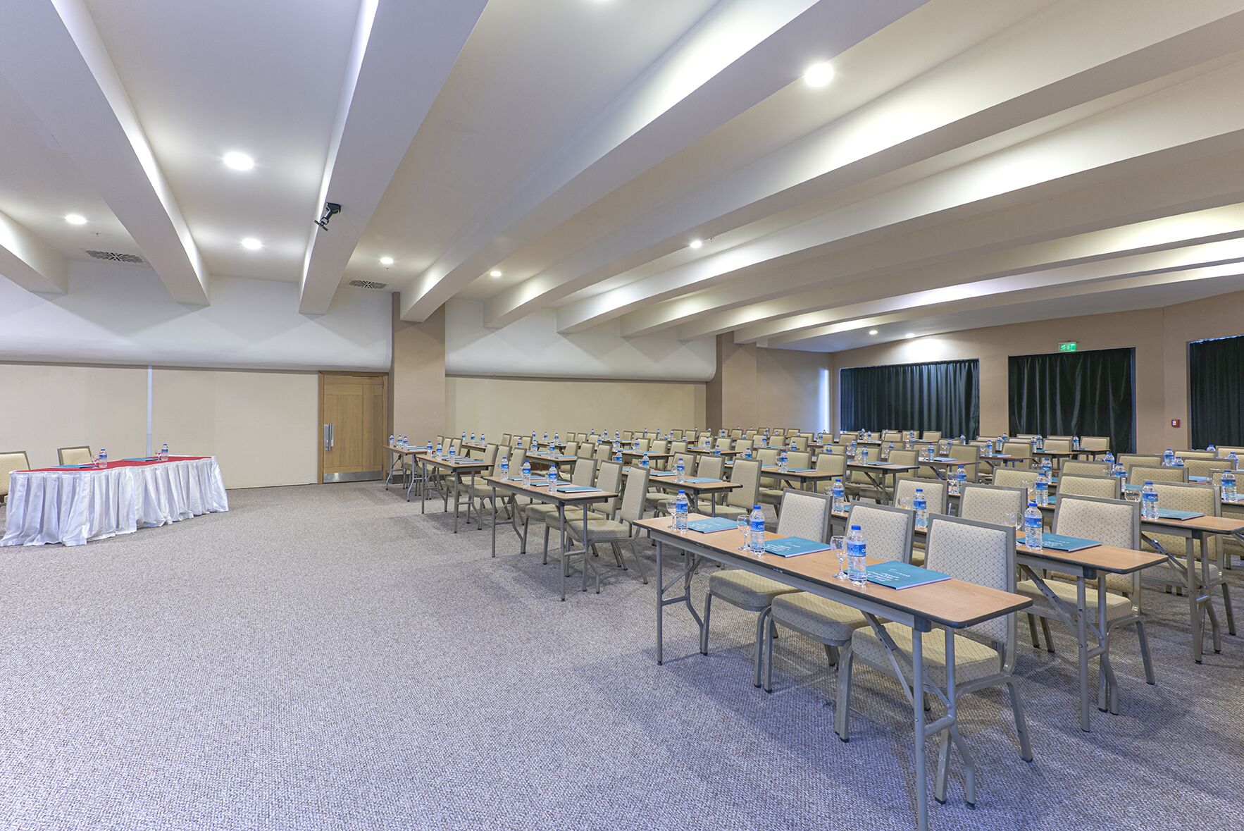 Un salón de conferencias con filas de mesas y sillas, equipado con botellas de agua y carpetas.