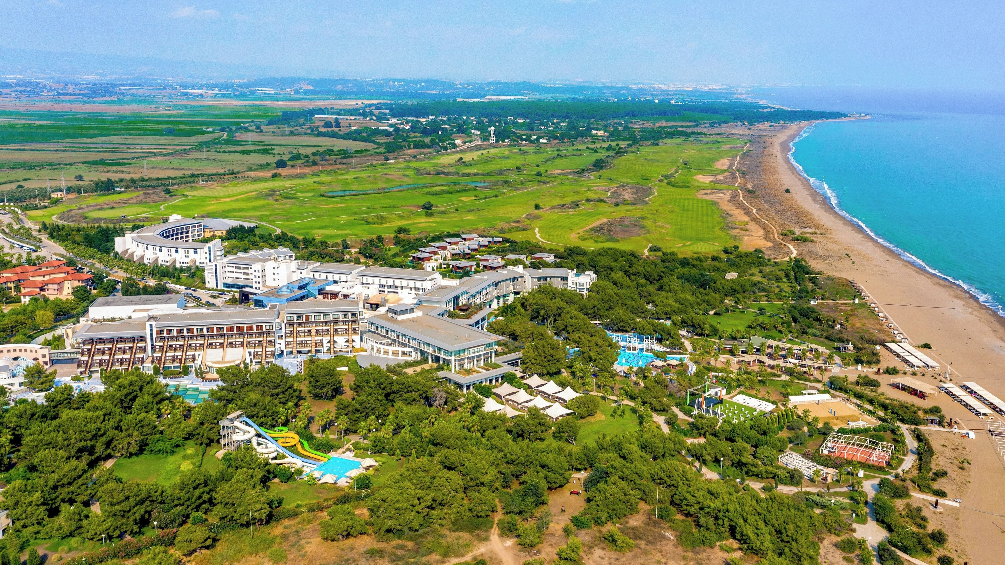An aerial view of a coastal resort with multiple buildings, a beach, and a golf course.