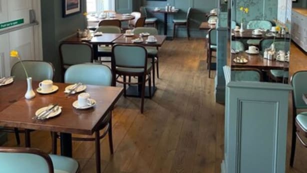 A restaurant with wooden tables and chairs, a green wall with a television, and a patterned wallpaper section. - The Beach Hotel (Brighton)