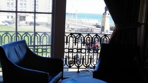 A room with a view of a cityscape through large windows, a balcony with wrought iron railings, and two chairs. - The Beach Hotel (Brighton)
