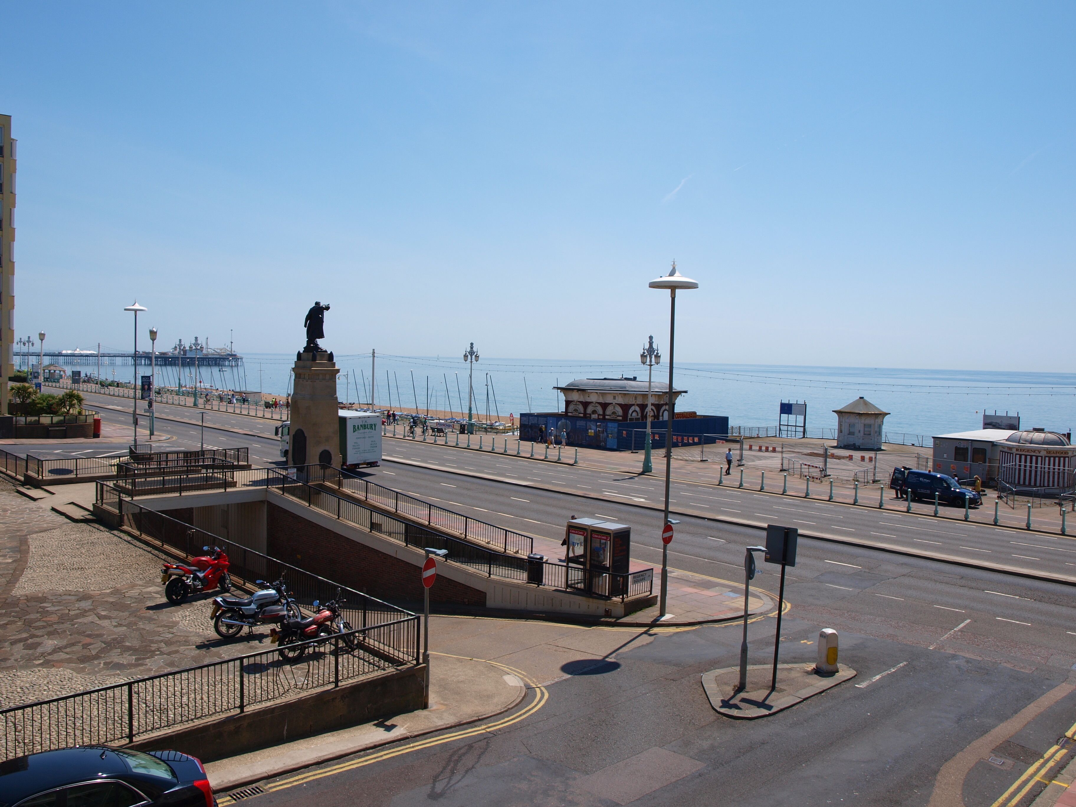 Una carretera costera con una estatua, una parada de autobús y vistas al mar.