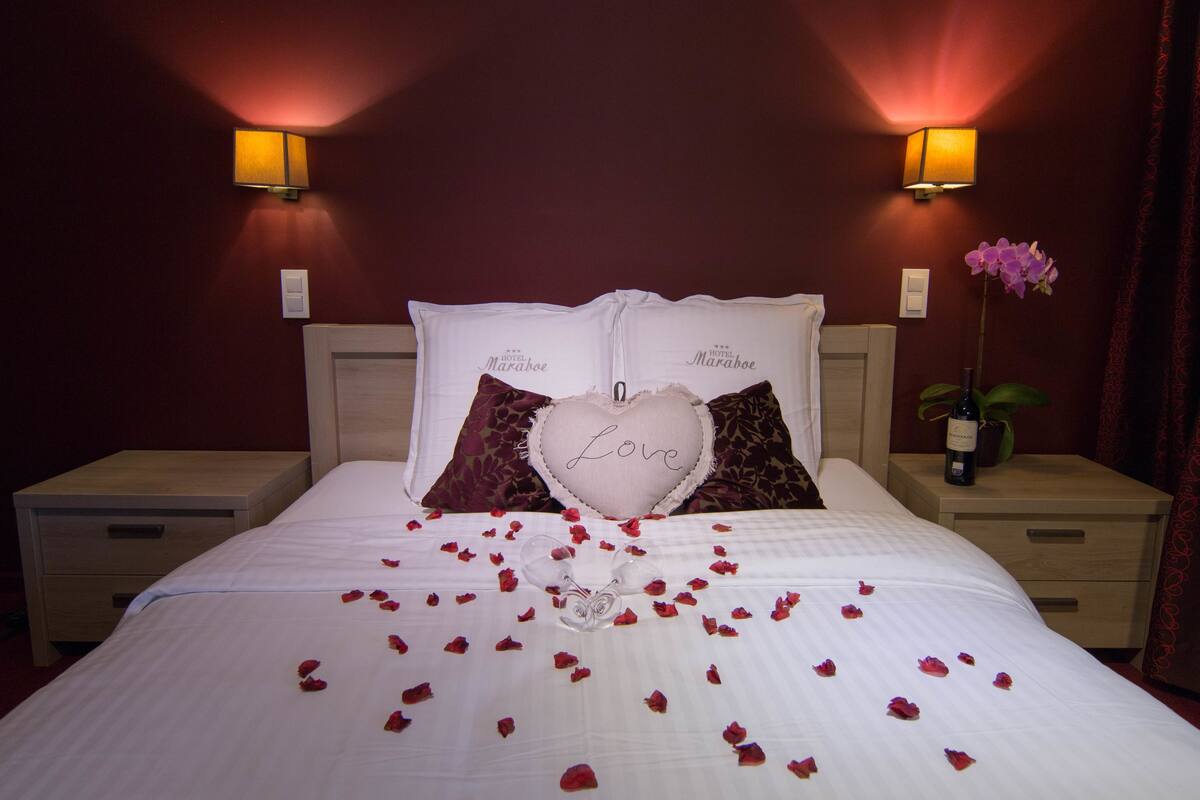 A hotel room with a bed, two nightstands, a potted orchid, and a bottle of wine.