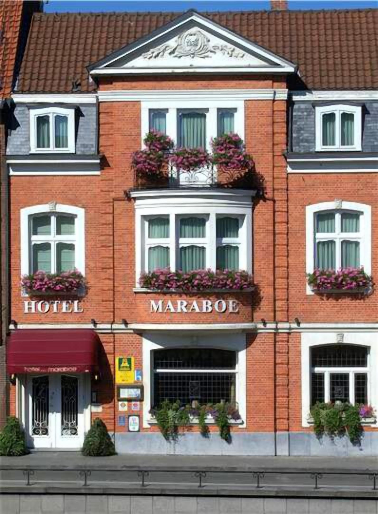 A two-story hotel with a red brick facade, white trim, and a central entrance with a maroon awning.