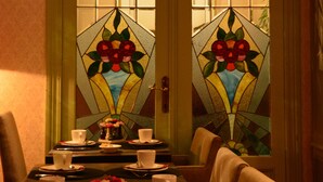 A dining area with a table set for four, a vase with flowers, and a door with stained glass windows. - Hotel Maraboe (Bruges)