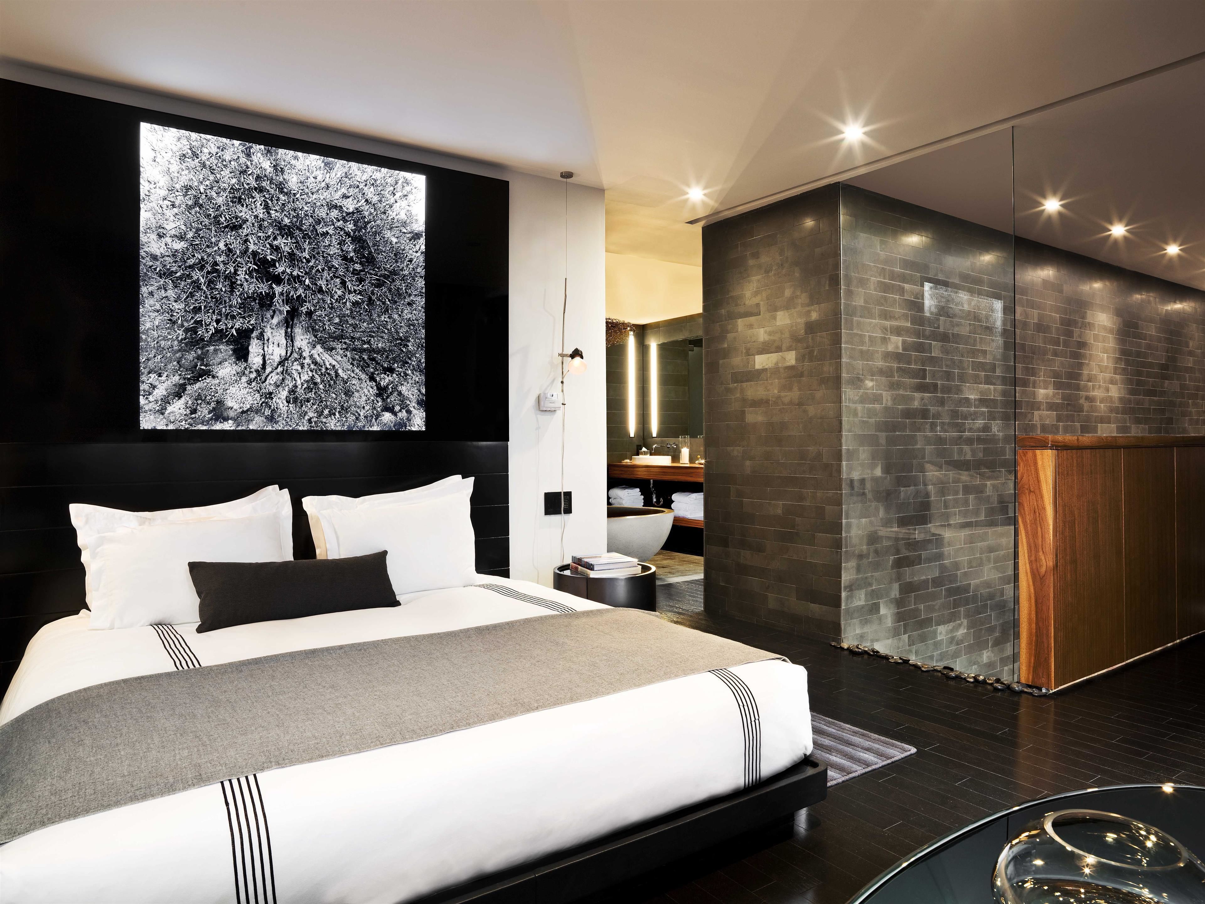 A modern bedroom with a large bed, a wall-mounted TV, and a bathroom with a stone wall and wooden cabinet.