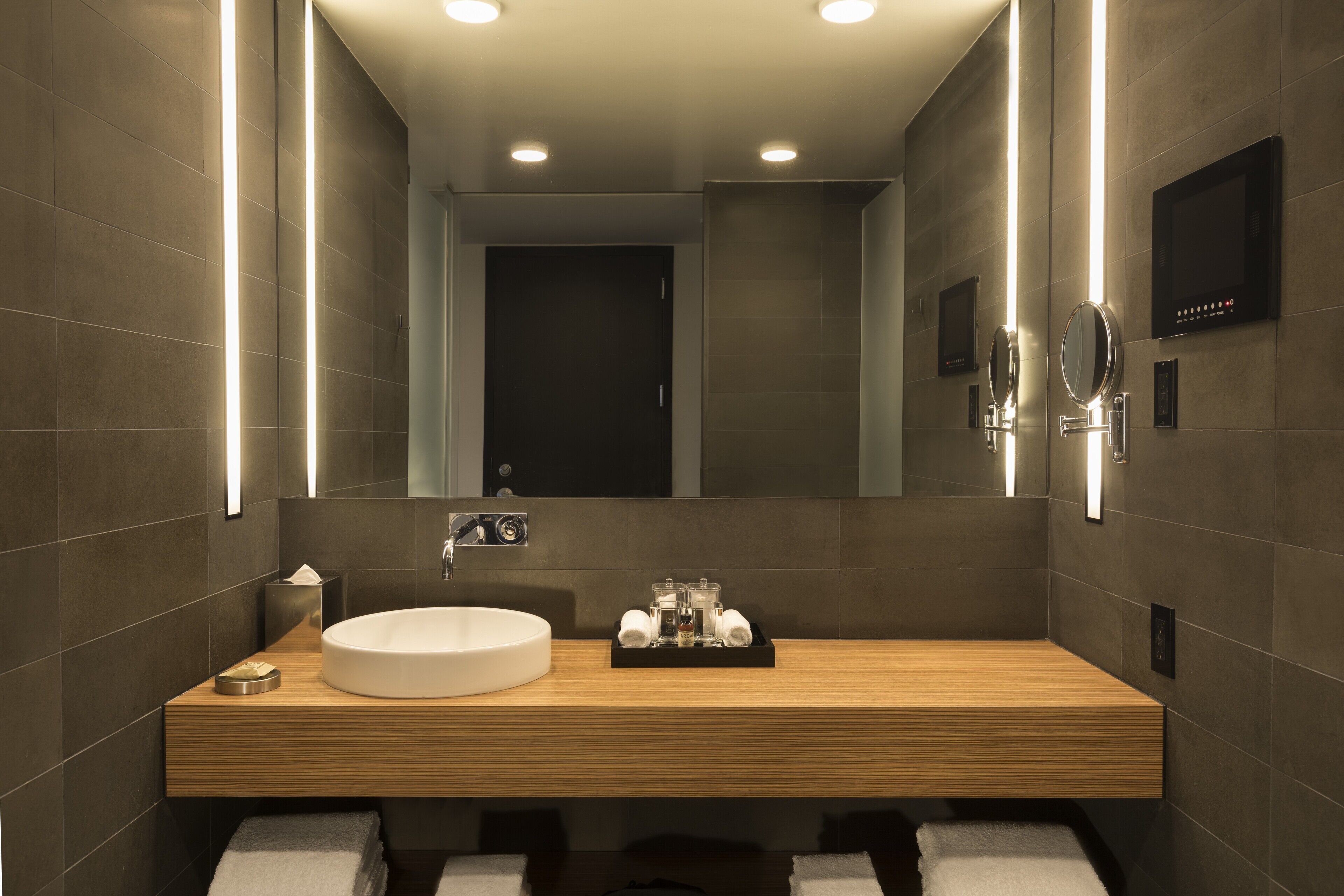 A modern bathroom with a wooden vanity, a round sink, and a large mirror.