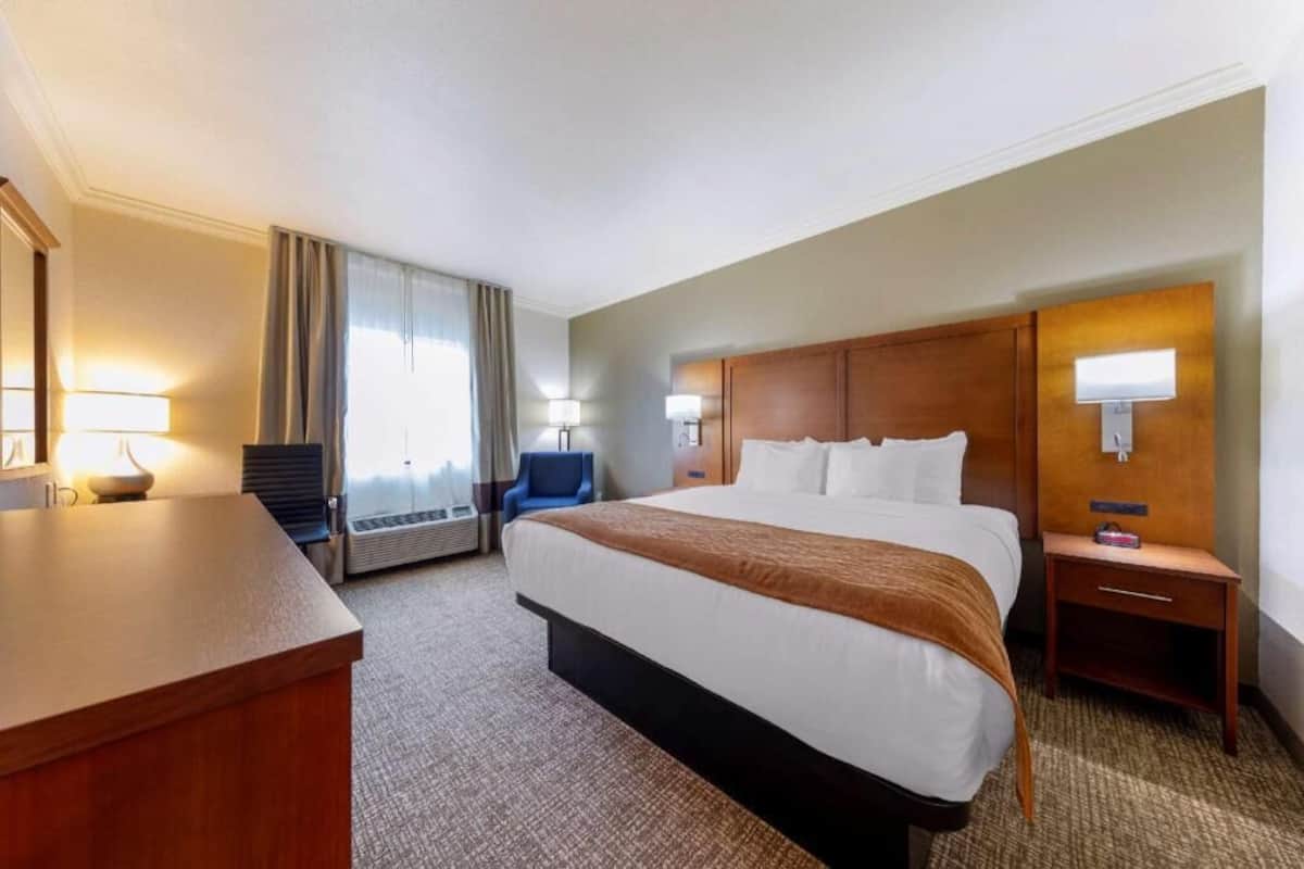 A hotel room with a bed, bedside tables, a desk, a chair, and a window with curtains.