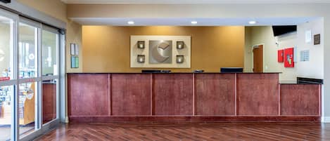Un espace d’accueil avec un comptoir en bois, une grande œuvre d’art encadrée au-dessus, et une porte vitrée donnant sur l’extérieur.