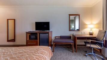 A hotel room with a bed, a desk with a computer, a television, a chair, and a lamp.