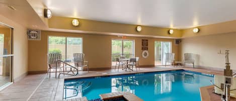 Un área de piscina con suelo de baldosas, un jacuzzi y varias sillas y mesas.