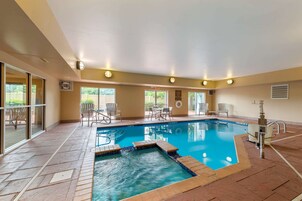 An indoor swimming pool with clear water, surrounded by tiled flooring and equipped with a hot tub.
