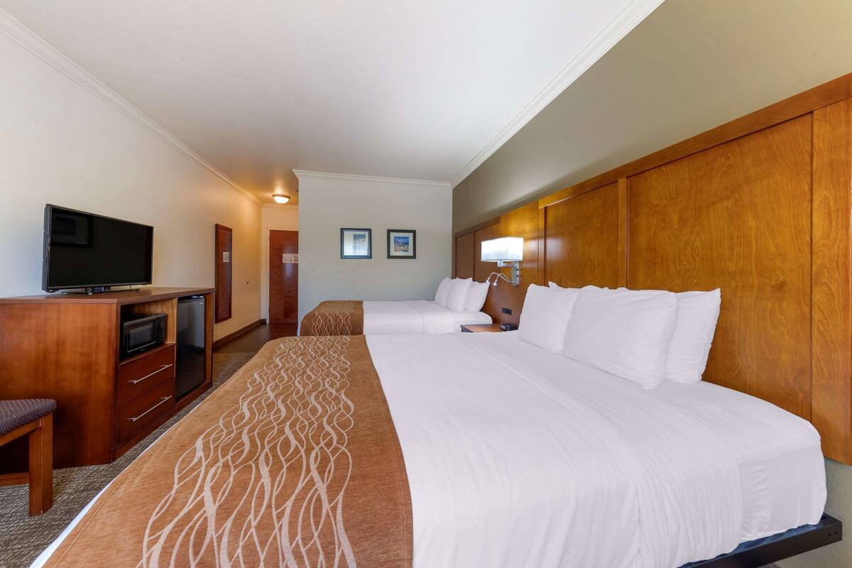 A hotel room with a large bed, a desk with a television, and a wooden headboard.