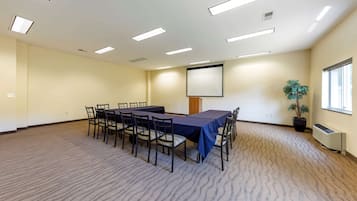 A conference room with a long table, chairs, a projector screen, and a potted plant.