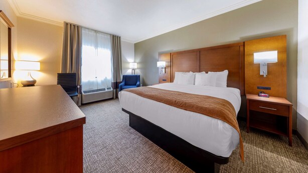 A hotel room with a large bed, a desk, a chair, a nightstand, and a lamp. - Comfort Inn Huntsville Research Park (Huntsville)