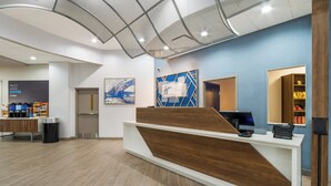 A modern reception area with a wooden reception desk, a digital screen, and a coffee station.