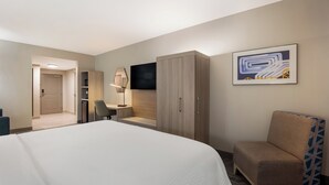 A hotel room with a large bed, a desk with a chair, a wardrobe, and a TV on the wall.