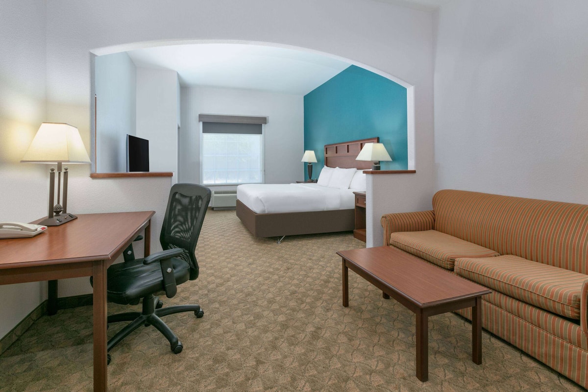 Una habitación de hotel con una cama, un escritorio con lámpara, una silla, un sofá y un espejo grande.