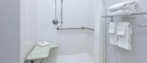 Un área de ducha moderna con puerta de cristal, barra de apoyo, toallero blanco y un pequeño banco.