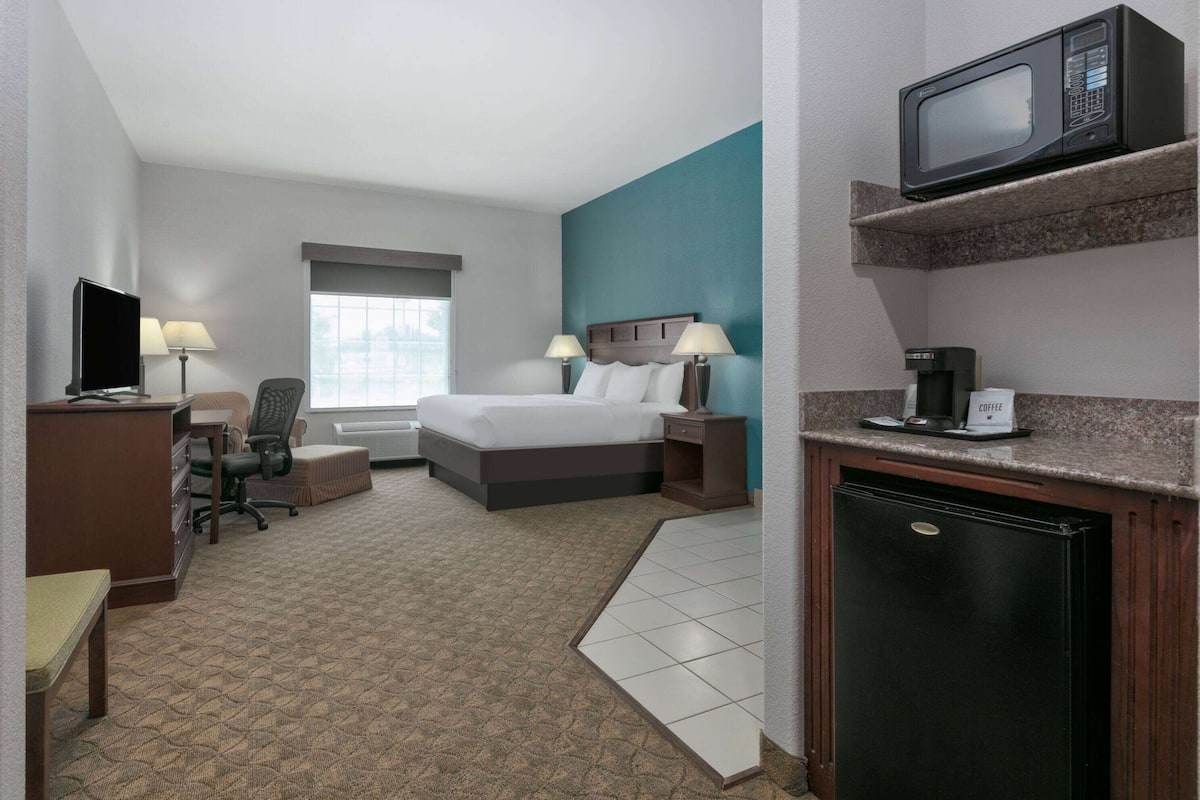 Habitación de hotel con cama, escritorio, silla y una kitchenette con microondas y cafetera.