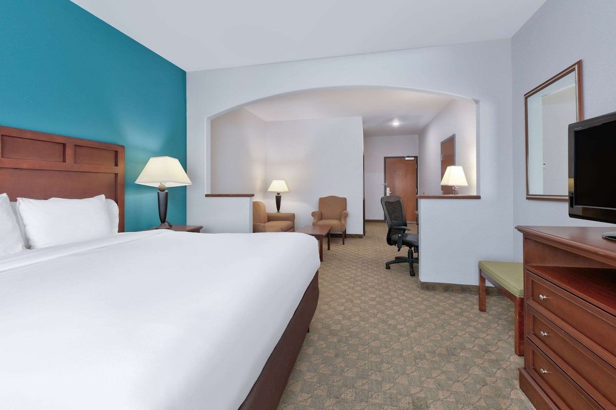 Habitación de hotel con una cama grande, dos sillones, un escritorio, un televisor y un espejo.